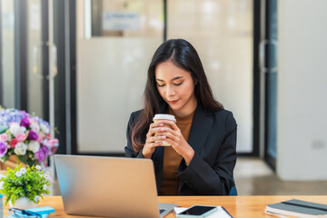 Front view of a beautiful businesswoman drink coffee sitting at the office with a laptop on the table.