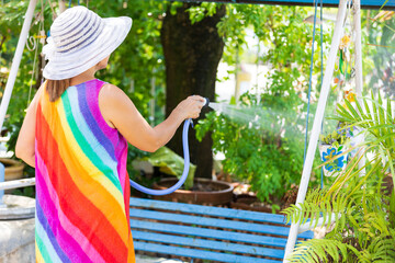 Naklejka na ściany i meble back view woman wearing hat with rainbow dresses, holding hose and water the plants