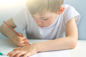 Focused preschooler little boy 5-6 years painstakingly draws drawing by pencil. Doing homework, drawing, education and child development. Childs creativity and art