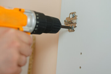 a man tightens a screw with a screwdriver in a door hinge on a white cabinet door