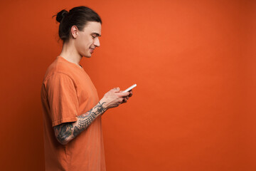 Young white man with tattoo smiling while using cellphone