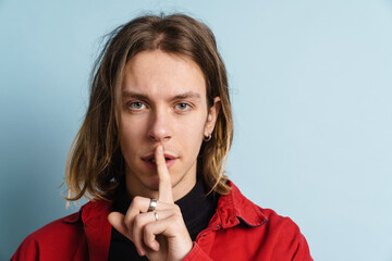Young white man wearing red jacket showing silence gesture at camera