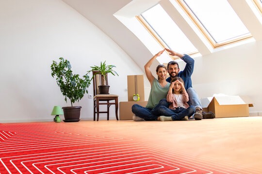 Floor heating concept - portrait of happy family sitting on warm parquet with floor heating and pipes.