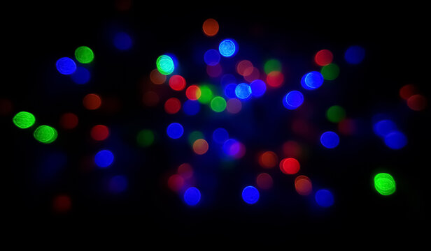 Beautiful abstract blur bokeh background of shiny colorful glowing small bubble like small circular decoration bokeh light bulbs blinking on blurry black night. Christmas and new year evening.