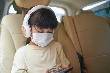 Asian little child girl wearing medical protective mask using and watching on smartphone while sitting on the car during Covid-19