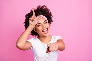 Portrait of brunette optimistic lady show loser sign wear white t-shirt hairband isolated on pastel pink background