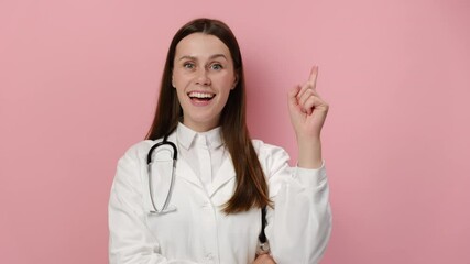 Portrait of thinking pondering doctor woman in medical white coat and stethoscope having idea moment pointing finger up, isolated on pink studio background. Smiling happy nurse showing eureka gesture