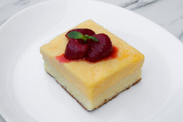 Gourmet dessert presentation. Closeup view of a cheesecake decorated with strawberries on a white dish on the table. 
