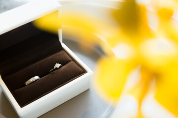 A white ring box with a silver pair of rings is placed on a disc, with a fuzzy yellow flower in the foreground