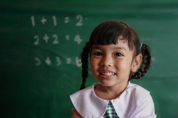 Asian little girl child in class standing confidently in front of a blackboard in mathematic class.