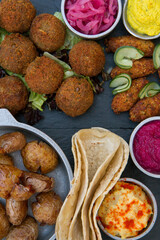 Vegan cuisine. Closeup view of fried potatoes, vegan fried kibbehs, lentil falafels, onion pickles, garbanzo, beets and carrot hummus, and corn tortillas on the table.