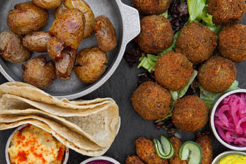 Vegan cuisine. Top view of fried potatoes, vegan fried kibbehs, lentil falafels, onion pickles, garbanzo, beets and carrot hummus, and corn tortillas on the table. 