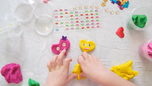 Holiday crafts. Child playing with colorful modeling clay sculpting heart figure with beads and sequins . Home Education game with clay. Early development concept