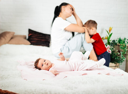 young woman sits with her two children, postpartum babies