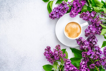 Morning cup of cappuccino with foam and branch of blooming purple lilac with green leaves on textured grey background. Coffee break. Slow life concept. Spring flowers. Flat lay, top view, copy space. - obrazy, fototapety, plakaty