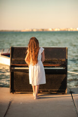 Beautiful girl in a white dress plays the piano on the pier by the sea