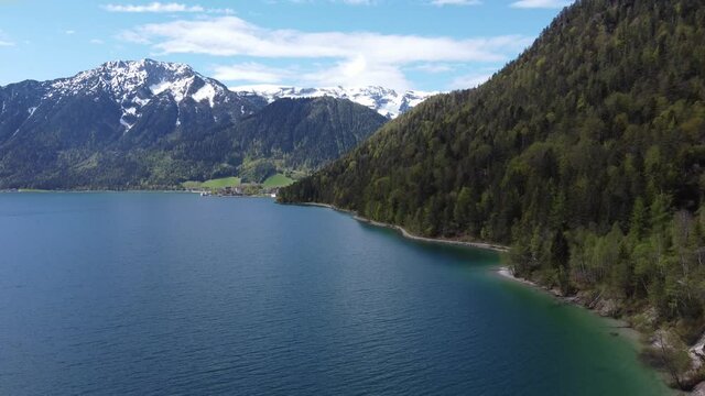 Hiking trail along the lake surrounded by Alps mountains. Aerial view of water and snow covered peaks.