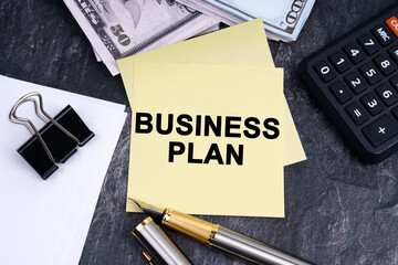 On the table is a calculator, a pen, money and stickers with the inscription - Business plan