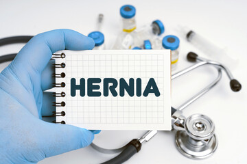 There is a stethoscope on the table, the doctor holds a notebook in his hand with the inscription - HERNIA