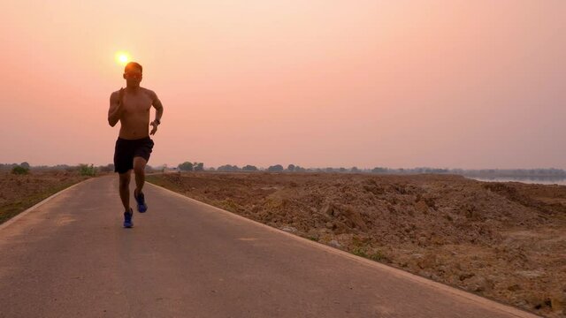 Silhouette of Young man running sprinting on road. Fit runner fitness runner during outdoor workout with sunset background. 4K