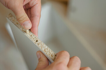 a man inserts a furniture dowel into a hole in a white board