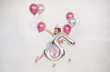 happy little birthday girl dancing with balloons and foil number five on a white background