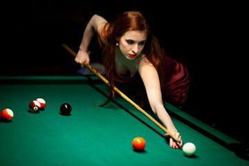 Woman aiming for the billiard table in dark room