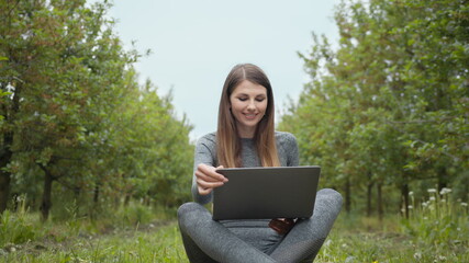 IT specialist working at self isolation outdoors. Women engaging in business or freelance at nature or fresh air at amazing sun light. Girl sitting in park or forest, opening laptop on nature.