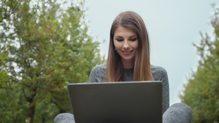 Woman opening laptop computer and starting to type on keyboard, trees at nature. Women engaging in business or freelance at nature or fresh air at amazing sun light. Girl sitting in park or forest