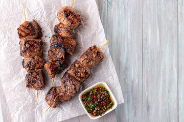 Grilled beef meat skewers with chimichurri sauce, horizontal, top view, copy space