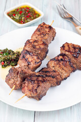 Grilled sirloin tips or beef meat skewers with chimichurri sauce, on white plate, vertical