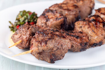 Beef meat skewers with chimichurri sauce, on white plate, horizontal, closeup
