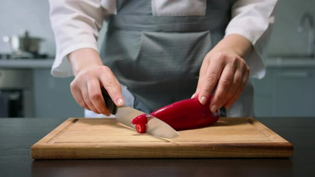 Female hands cut red ramiro pepper into round slices by knife on wooden board