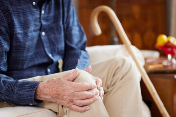 Close Up Of Senior Man Sitting On Sofa At Home Suffering With Knee Pain From Arthritis