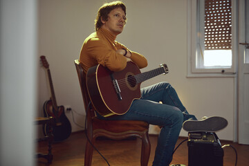 Male musician playing acoustic guitar on the amplifier in retro vintage room.