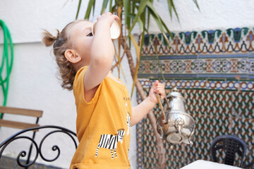 Toddler girl drinking tea in the cafeteria with an antique teapot.