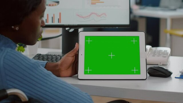 Disabled handicapped african woman employee in wheelchair looking at tablet with green screen chroma key mock up izolated display analysing graphs, financial statistics working in start up office