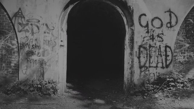 Black and white footage of dark gate with God is dead graffiti on the wall.