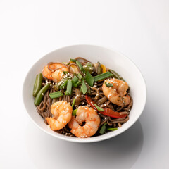 Wok Brown Spaghetti with king prawns, vegetables and sesame seeds. Seafood plate, Spicy oriental dish on white background. Pan-Asian cuisine. Soft focus.