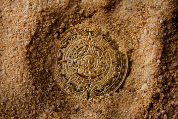 Ancient aztec coin laying in sand upper view.
