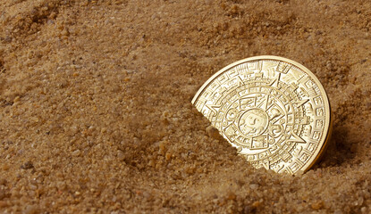 Golden ancient aztec coin laying in sand angle view