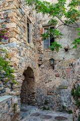 Fototapeta na wymiar Byzantine Street with Traditional Alley with Arch in Monemvasia Island, Peloponnese, Greece. Medieval Style Stone House with Big Windows Above the Footpath.