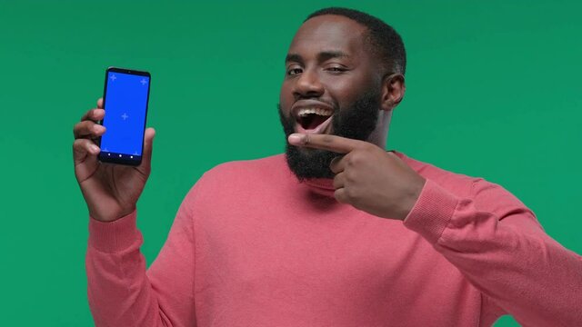 Excited young african american man in casual posing isolated on a green background in the studio pointing finger on mobile phone
