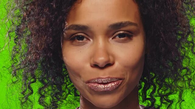 Gorgeous curly dark skinned woman with sequins and glitter on lips folds lips, blows air kiss, expresses love, waits for true feelings to come, sends mwah, isolated on chroma key background