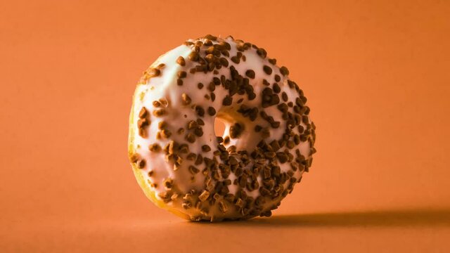 White chocolate donut with almonds topping rotating zooming in and out on orange background.