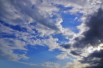 The bright sun hid behind light white clouds in the blue sky.
