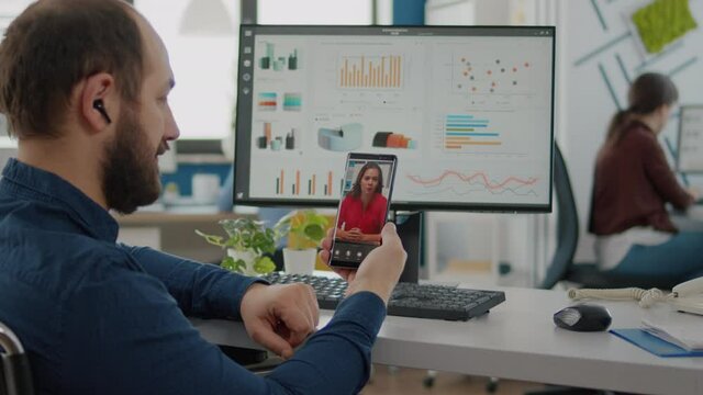 Disabled, paralyzed invalid man holding smartphone talking on webcam with coworker during video conference, videocall, online meeting with business partner sitting in wheelchair in start up office