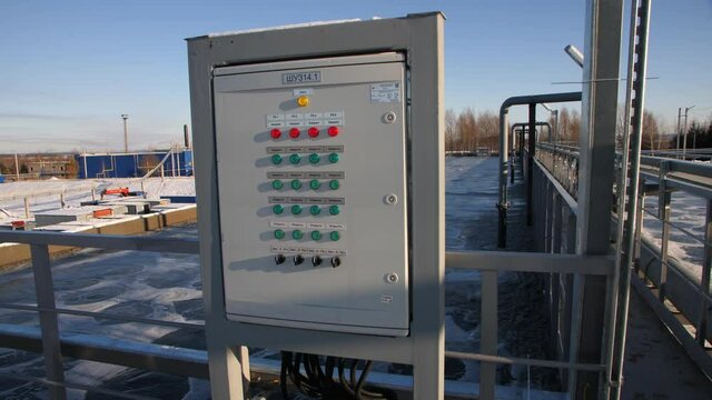 Control panel with bright buttons near reservoir for aeration at contemporary waste water treatment plant on winter day