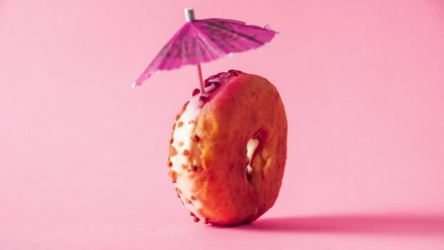 White chocolate donut with almonds topping and a decoration umbrella rotating zooming in and out on pink background.