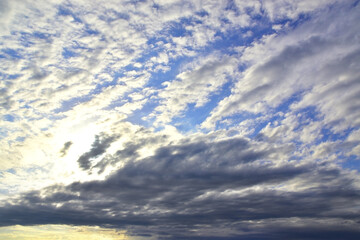 Obraz premium The bright sun hid behind light white clouds in the blue sky.